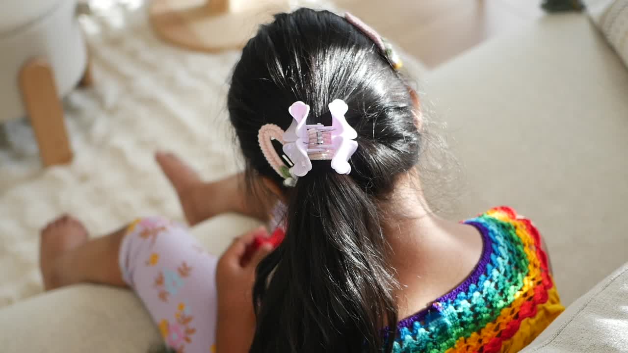A child with a ponytail and rainbow sweater