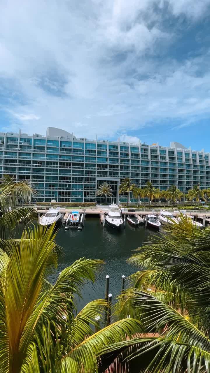 Yacht di lusso ormeggiati in marina vicino a un moderno condominio. Vista dall'alto di barche in un porto con un grande edificio bianco in vetro e palme.