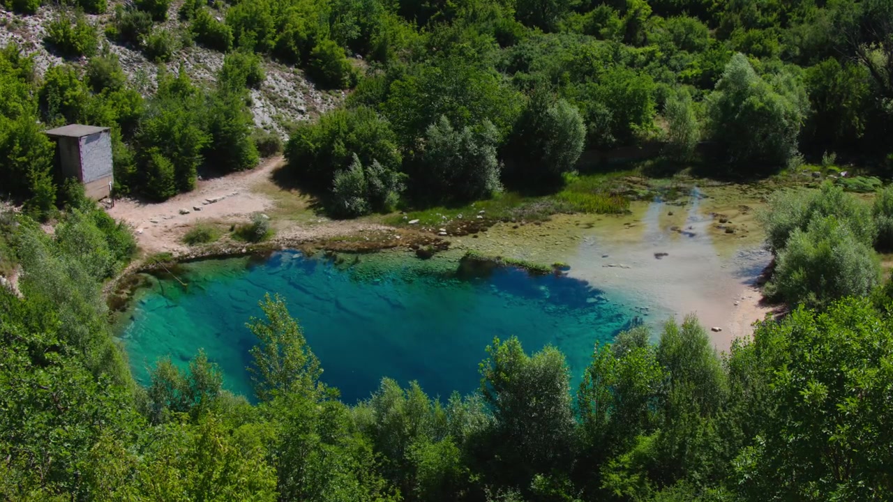 Sorgente turchese cristallina che forma la fonte del fiume Cetina vicino a Civljane, Croazia, circondata da vegetazione lussureggiante e aspro paesaggio carsico