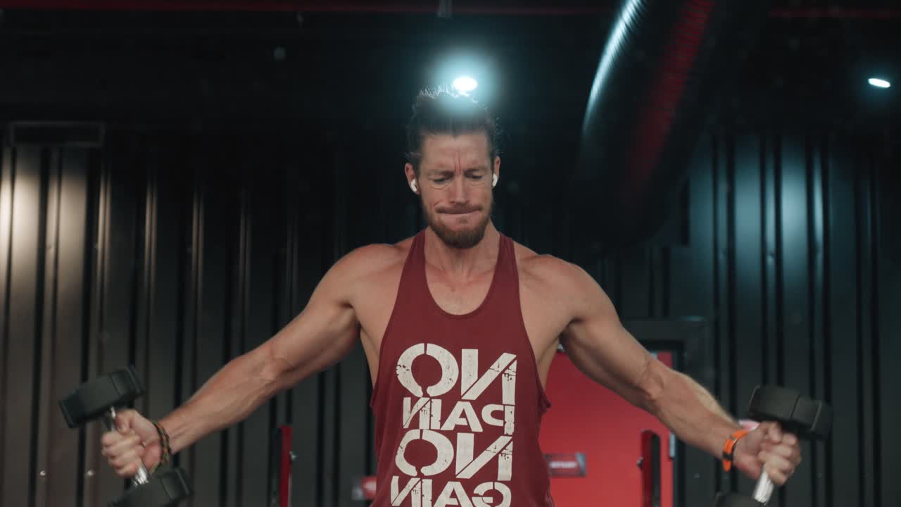 Hombre musculoso esforzándose con las últimas repeticiones de su entrenamiento con mancuernas