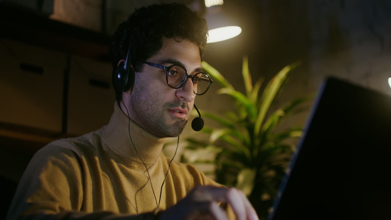 Mand arbejder sent om natten på bærbar computer med headset