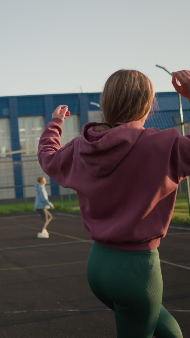 vista trasera de una mujer intentando servir voleibol pero haciéndolo incorrectamente con otros dos en el fondo, uno con capucha verde y otro con capucina azul, en la cancha de voleibol