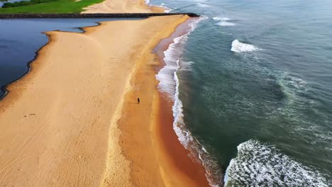 Drone-footage-of-Beach-with-a-backwater-opening-to-it-with-a-city-skyline-with-high-rises-in-backdrop