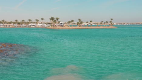 clear turquoise water over coral reefs with a beach and palm trees in egypt