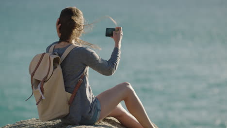 Cámara-Lenta-Atractiva-Mujer-Joven-Tomando-Fotos-De-La-Tranquila-Playa-Del-Océano-Usando-Tecnología-De-Cámara-De-Teléfono-Inteligente-Sentada-Relajada-Disfrutando-Del-Viento-De-Verano-Soplando-El-Cabello