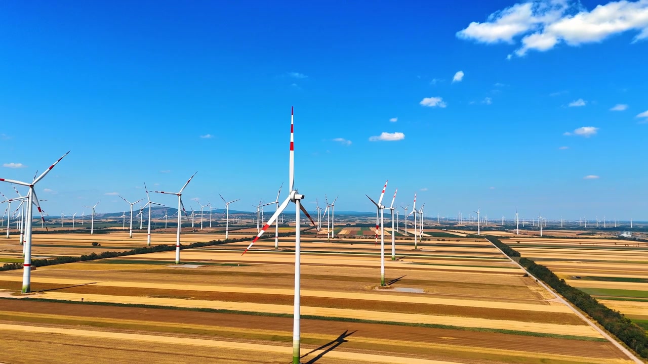 Windparkturbines staand in gouden geoogste velden. Luchtopname van duurzame elektriciteitsgeneratoren onder een helderblauwe lucht