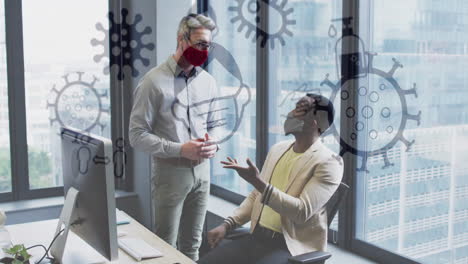 animation of virus icons over diverse businessmen with face masks talking in office