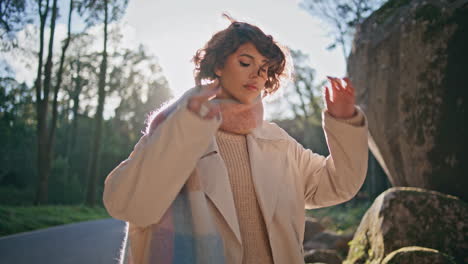 elegante turista posando bosques luz del sol a la moda vestido con abrigo de primer plano.