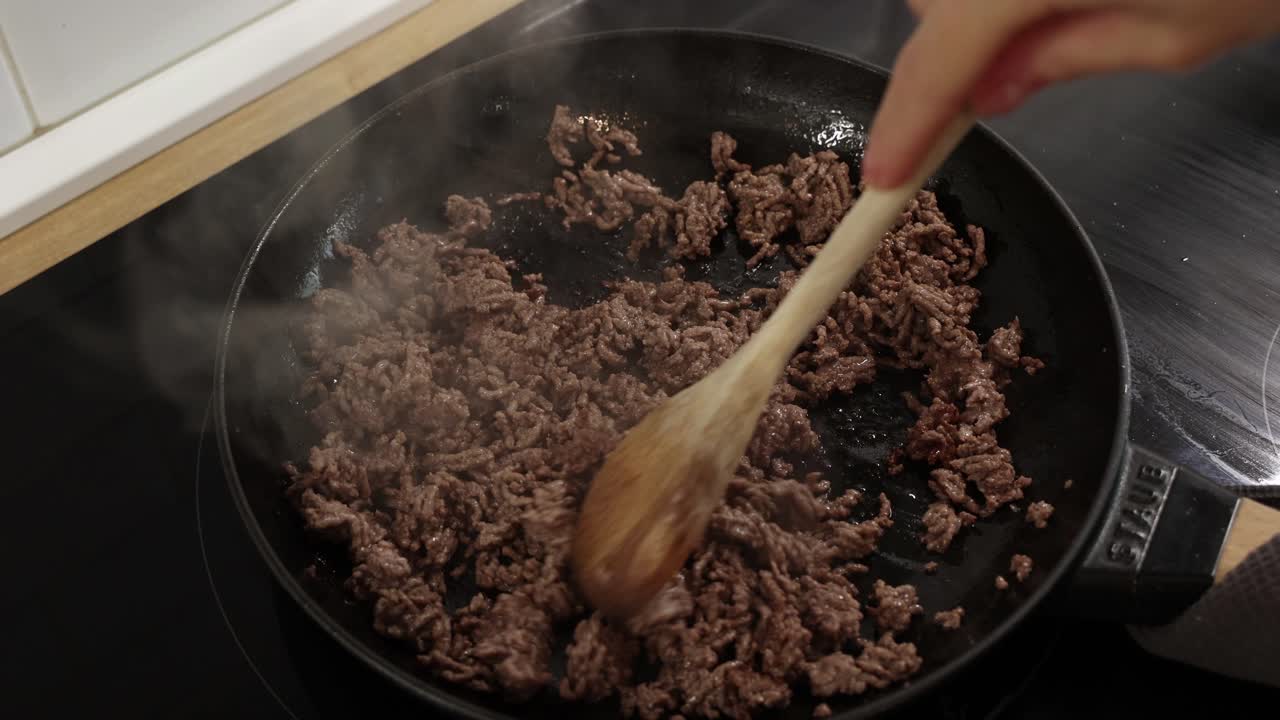 Daging sapi mentah cincang yang kecoklatan sedang diaduk di wajan panas dengan uap tebal saat dimasak.
