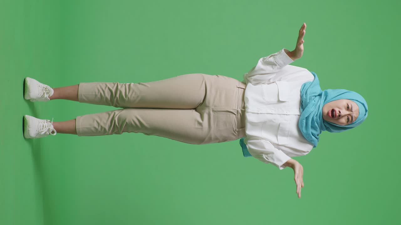 "아시안 무슬림 여성이 ""왜?""라고 물어보고 녹색 스크린 배경 스튜디오에서 의심스럽게 서 있습니다."