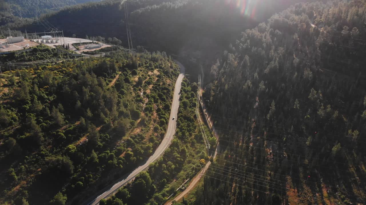 A lonely car driving at Jerusalem mountains aerial footage tracking drone shot, golden hour sun sunset on a lonely road between the forest.