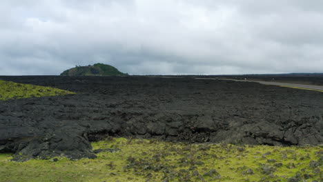 drone flyover black volcanic lava field with green shrubbery and mountain in distance, 4k