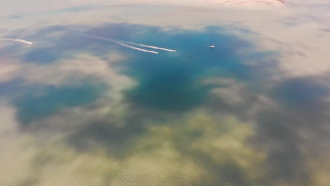 several small boats zooming across a large expanse of tropical waters with colours of olive green and navy blue spilling between the banks of submerged sand near gorgeous summer islands