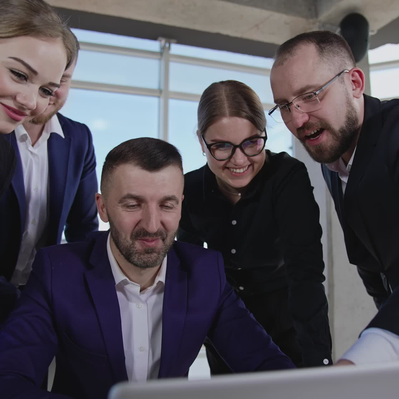 Creative team stand around boss sitting in front of computer. Happy positive young team working on idea in the office. Close up with gradual distancing