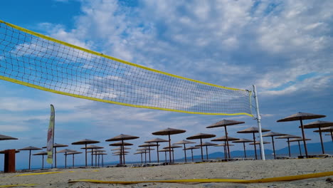 beach volleyball net near the sunbeds and straw beach umbrellas