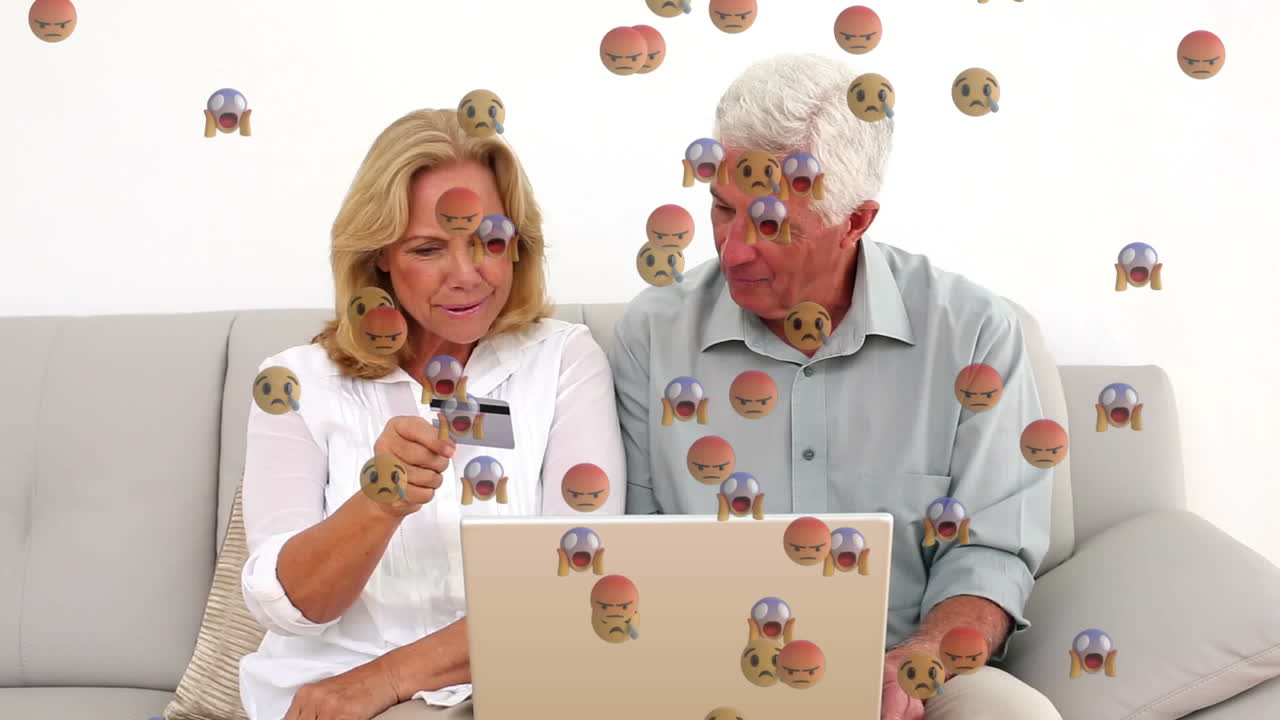 animación de iconos emoji aterradores sobre una pareja caucásica pagando con tarjeta de crédito usando una computadora portátil.