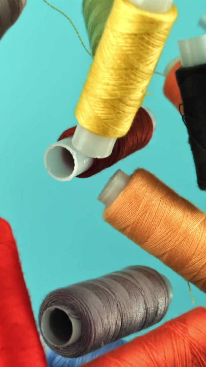Colorful Thread Spools Falling in Slow Motion on Blue Background