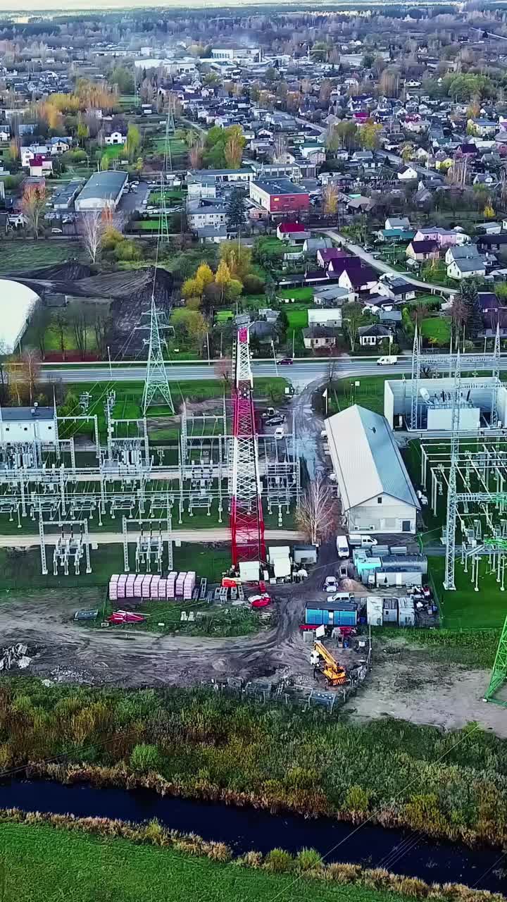Substation facility and high-voltage lines near residential town area from above, vertical
