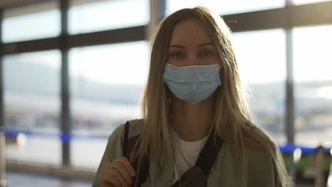 Portrait-of-a-beautiful-happy-blonde-woman-with-a-protective-mask-standing-at-the-airport