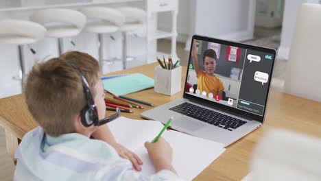 Schoolboy-using-laptop-for-online-lesson-at-home,-with-school-friend-and-web-chat-on-screen