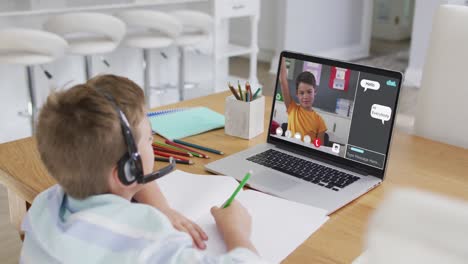schoolboy using laptop for online lesson at home, with school friend and web chat on screen