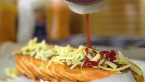 putting ketchup on hotdog topped up with cheese and onion