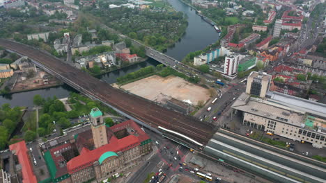 Toma-Aérea-Del-Río-Havel-Que-Atraviesa-La-Ciudad-Cerca-De-Rathaus-Spandau.-Vista-De-ángulo-Alto-Del-Tráfico-Alrededor-De-La-Estación-De-Tren.-Berlín,-Alemania