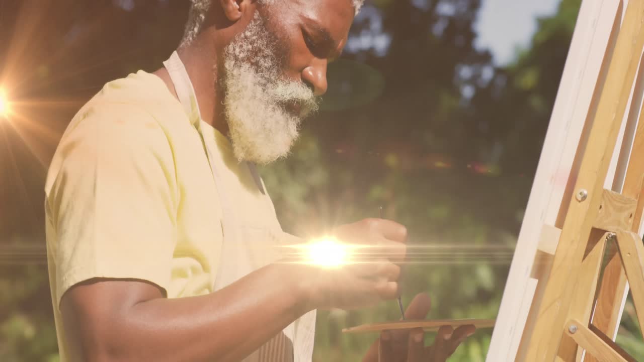 Animation of light trails over senior african american man painting on easel in garden