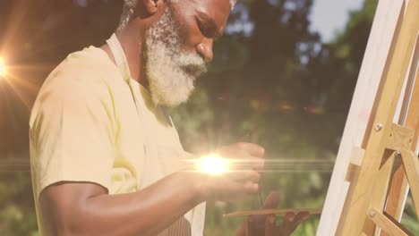 animation of light trails over senior african american man painting on easel in garden