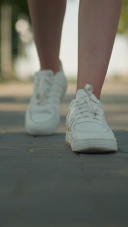 vista de cerca de la pierna de un individuo con zapatillas blancas caminando por un camino entrelazado bajo la cálida luz del sol, con un fondo borroso con árboles altos, vegetación exuberante y un entorno al aire libre sereno