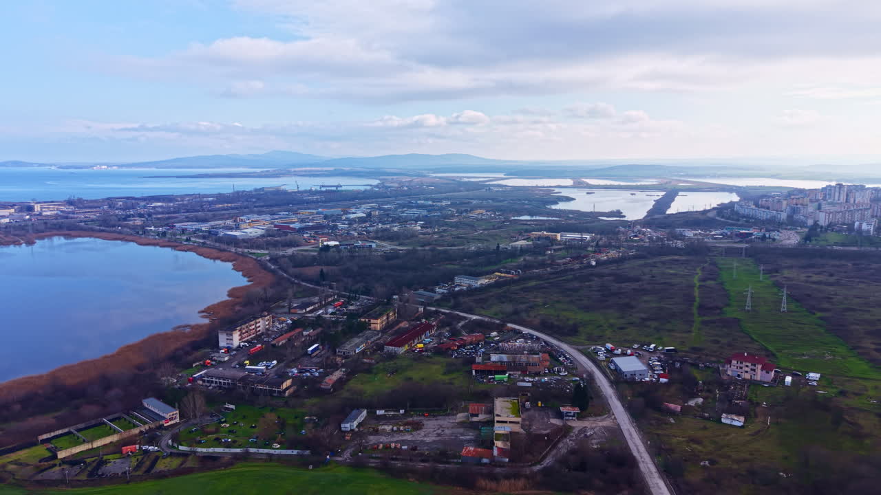 Utsikt över ett landskap med en sjö och stad i fjärran nära kusten under dagtid, med moln och grönska i förgrunden.