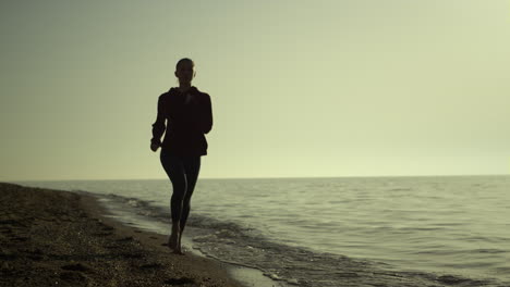silhouette woman running beach at sunset. girl jogging seacoast summer evening.