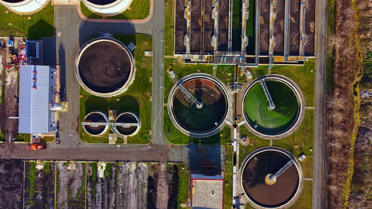 Water treatment facility shows different stages of wastewater processing in a large area with circular tanks located outdoors during daylight