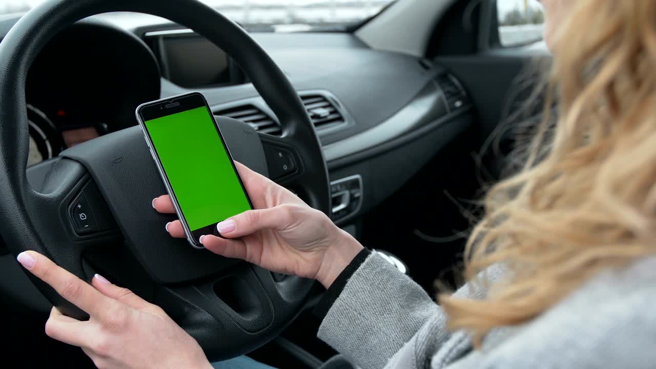 mujer se sienta en el coche moderno y usando el teléfono inteligente - manos de primer plano. pantalla verde. llave croma
