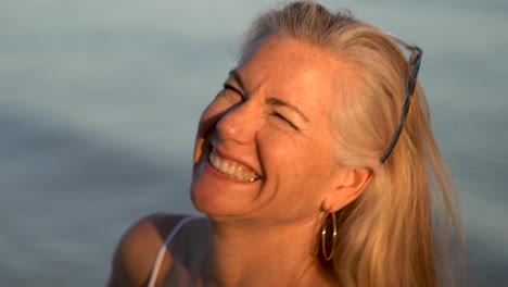 Closeup-of-mature-blonde-woman-with-gray-hair-playing-with-her-hair-and-looking-old-in-granny-glasses-and-laughing