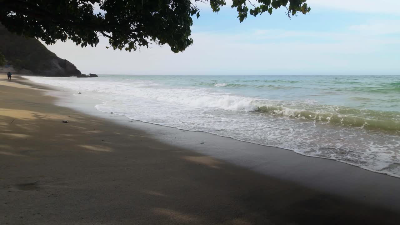 Silhouette of couple strolling along beach, watching waves splash tropical coastline