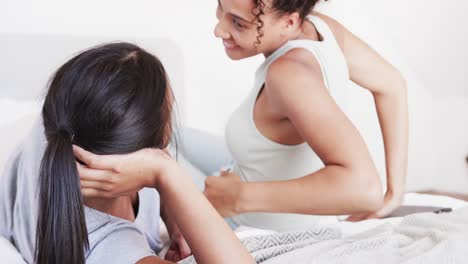 happy biracial lesbian couple lying on bed talking and smiling at each other, in slow motion