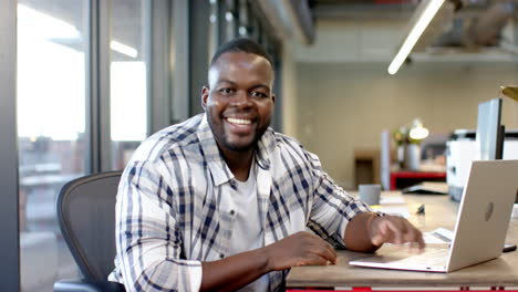 african american man smiling using laptop at desk in office