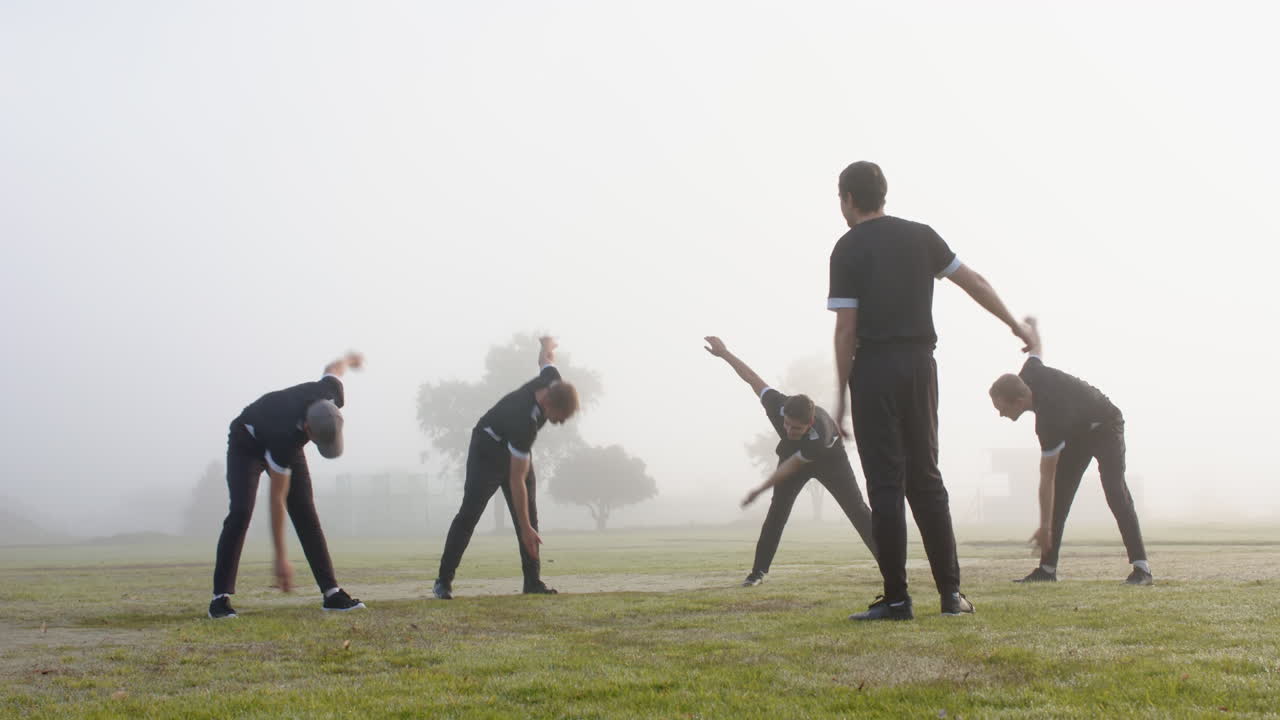 Cricket team warming up with stretching exercises on foggy field in morning