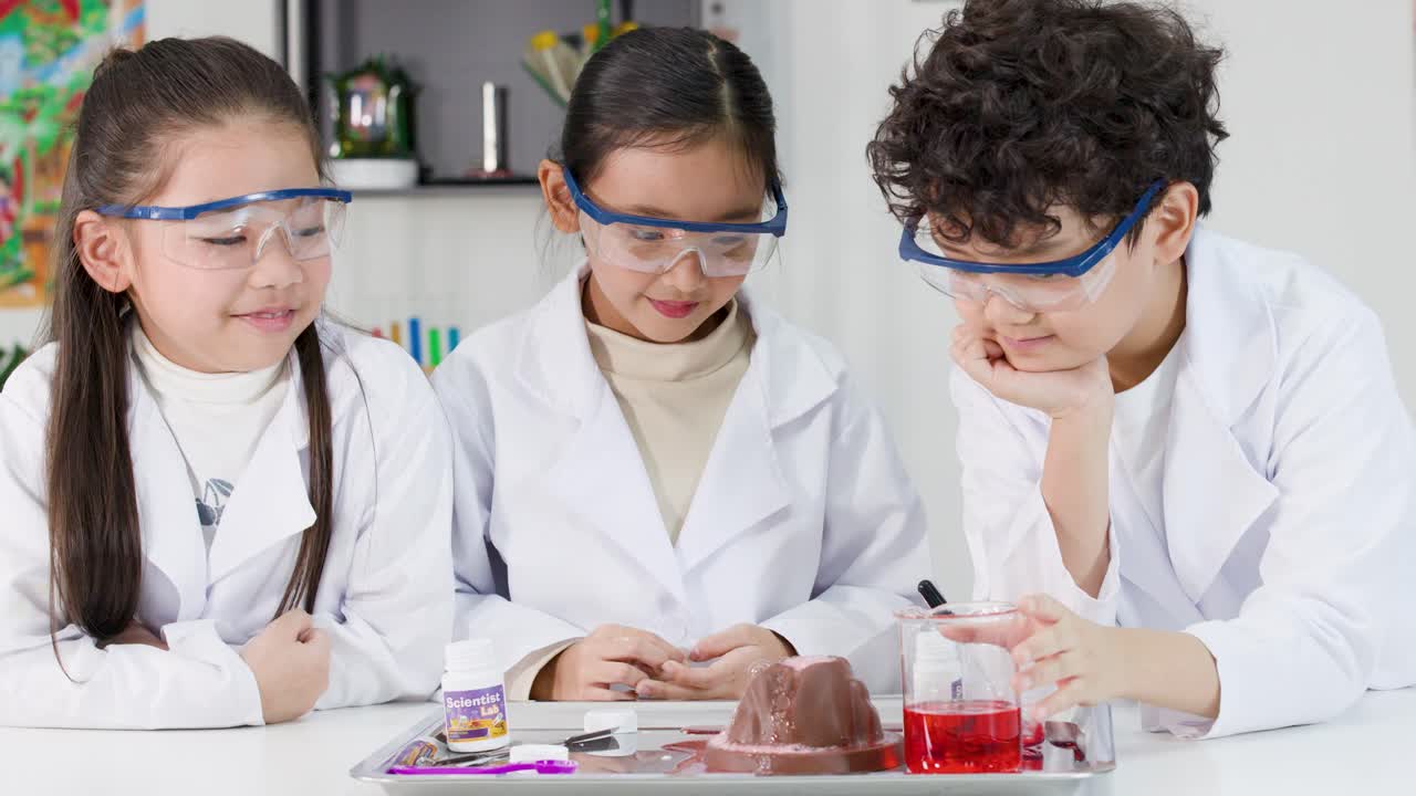 Tre studenti delle elementari indossano occhiali di sicurezza mentre eseguono un esperimento di reazione chimica in un'aula