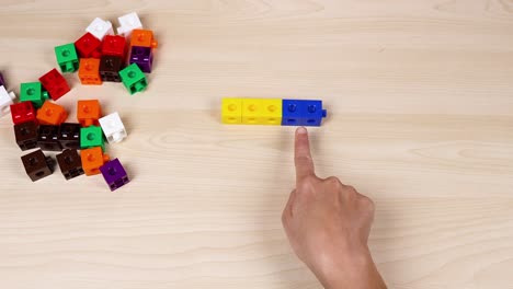 hand interacts with colorful linking cubes on table