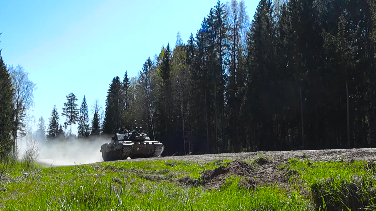 Awesome rare video footage of a large heavily armored British Challenger 2 4034 tank with a large cannon driving by on a dirt and dusty countryside forest road during summer sunny day, low angle video