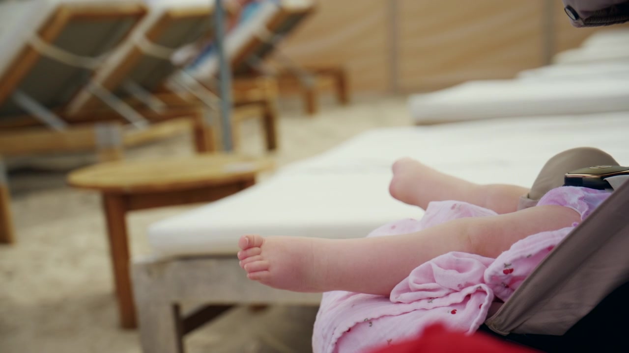 Baby feet resting on a sunbed with beach and lounge chairs in the background, capturing summer vacation and childhood relaxation