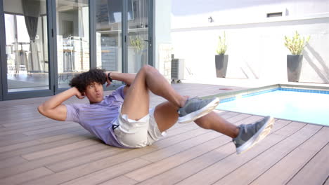 A-young-biracial-man-is-doing-sit-ups-by-the-pool-in-the-backyard-at-home