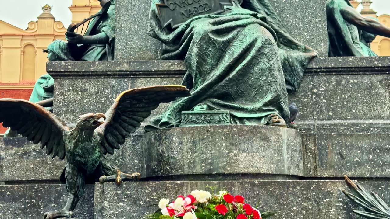 Pan down on the Adam Mickiewicz Monument in Krakow, Poland, from the bronze figure to the engraved pedestal and allegorical sculptures under an overcast sky.