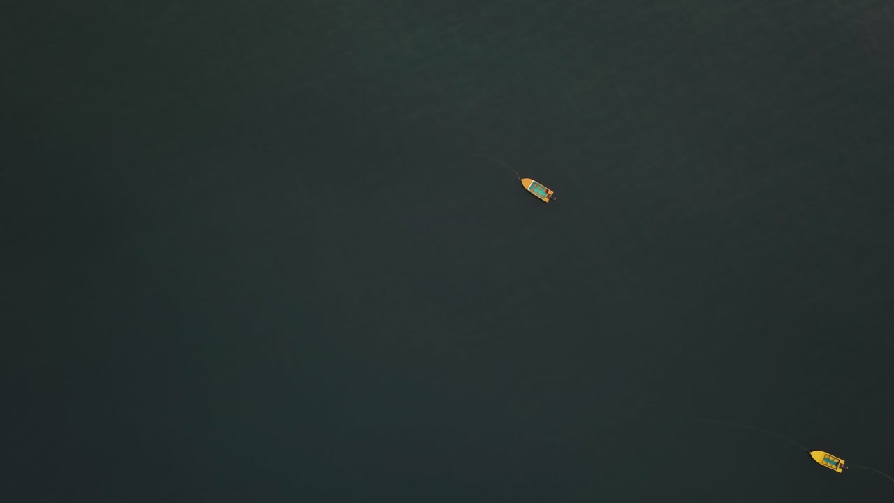 Top-down view of traditional wooden fishing boats anchored in dark blue-green ocean waters off the coast of Calangute Beach, Goa, India. Two small vessels float isolated in the Arabian Sea.