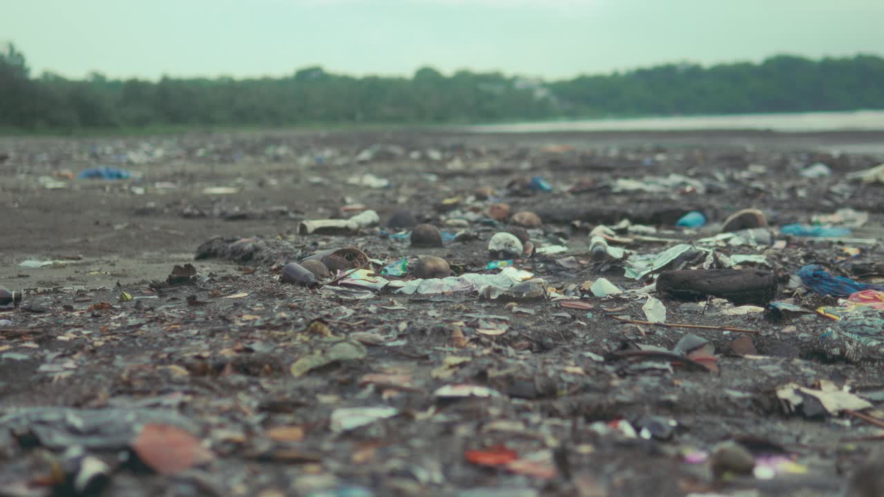 Wide view of a polluted shoreline covered with plastic bottles, fragments and debris showing environmental damage and ocean pollution near a coastal landscape