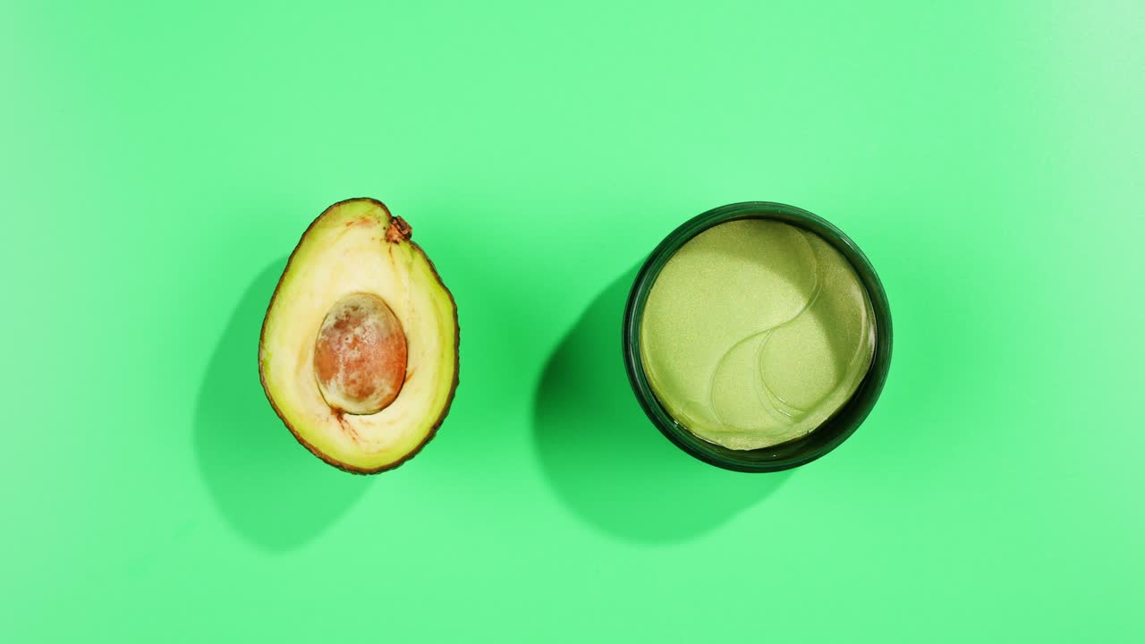 Fresh ripe avocados with cream and essential oil on green background with mint mentol, make up cosmetics