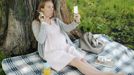 pregnant woman taking selfie in park with ultrasound photos