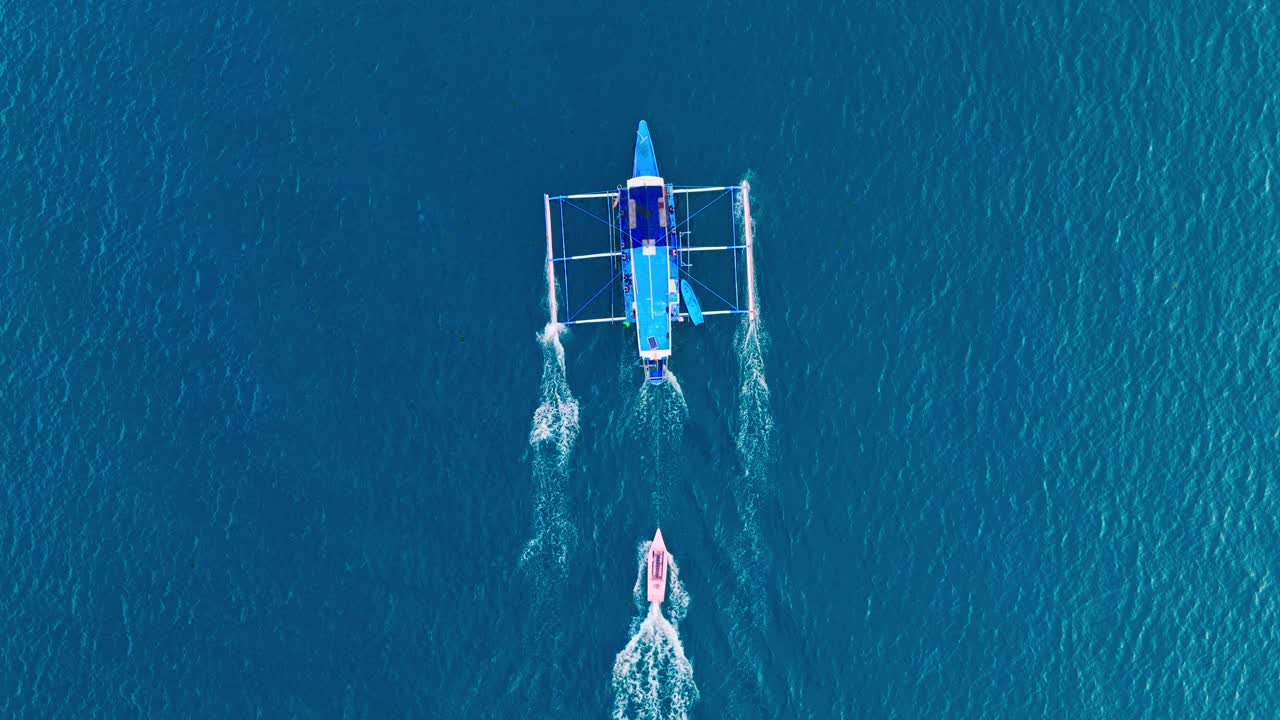Dronebillede oppefra af en stor udliggerbåd, der trækker en mindre lyserød båd over havet